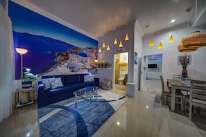 A modern living room with a large mural, a blue sofa, a coffee table, and a dining area with a wooden table and chairs.