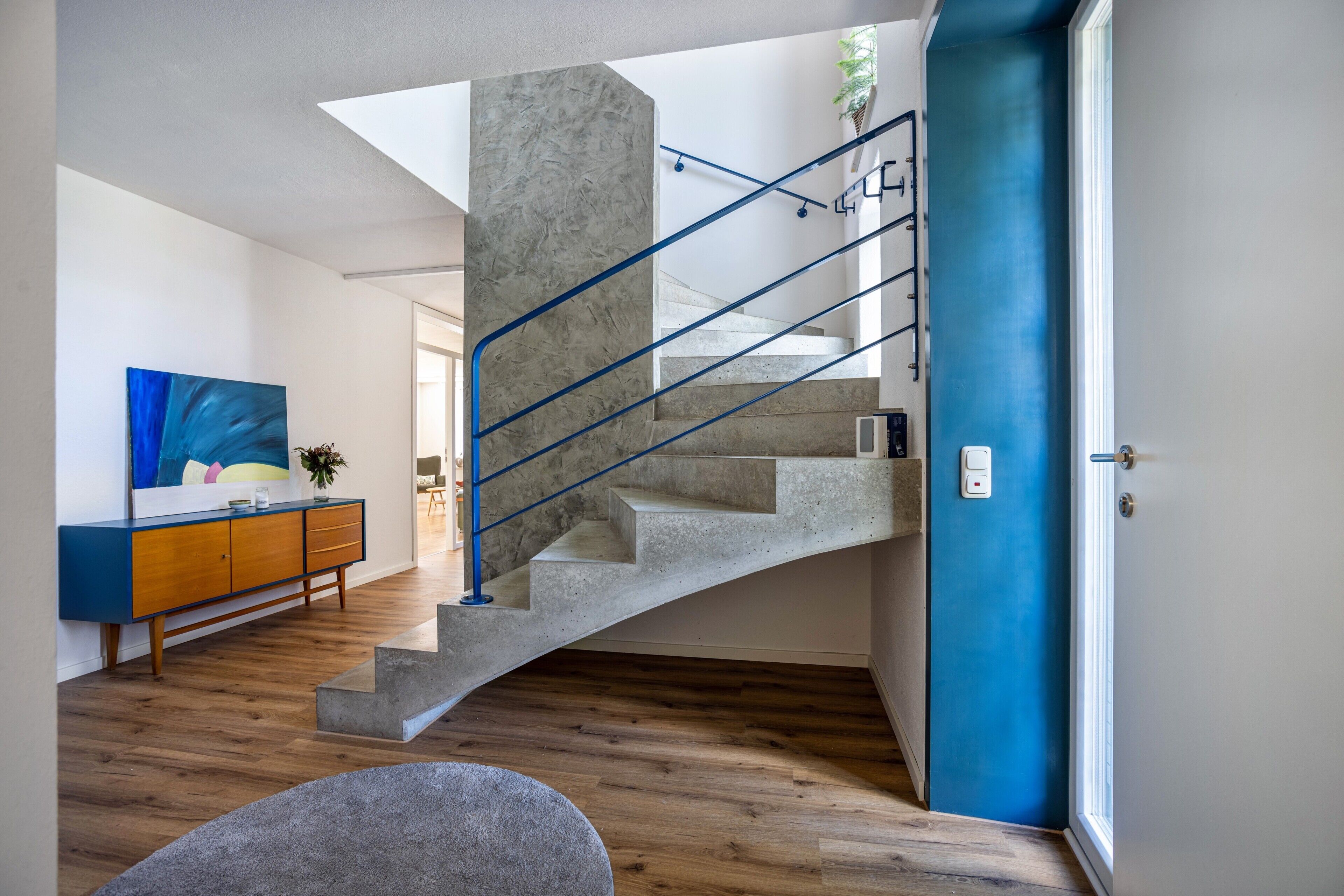 Um interior moderno com uma escada curva, uma porta azul e um chão de madeira.
