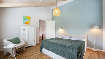 A bedroom with a bed, a chair, a small table, a wardrobe, and a painting on the wall.