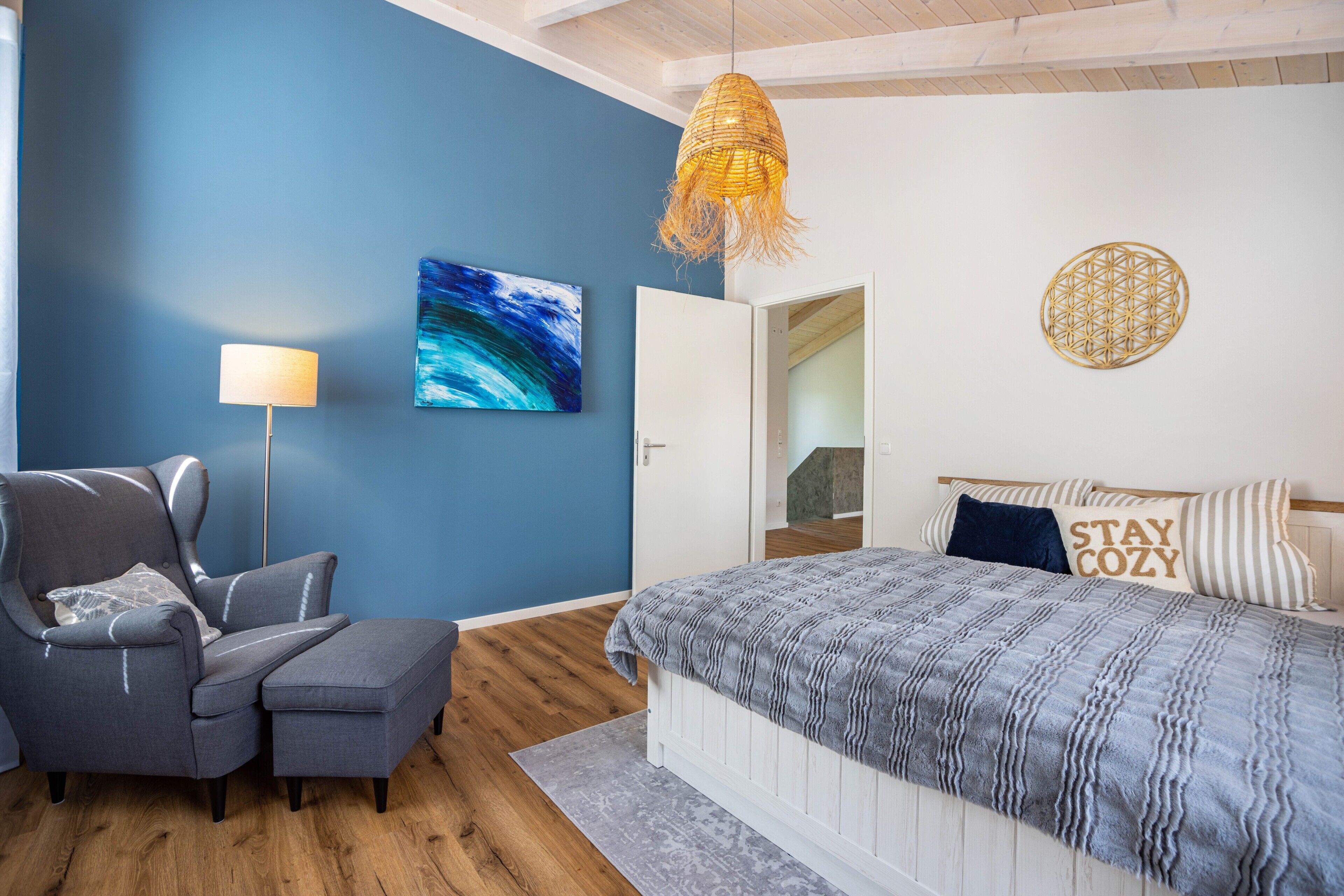 Une chambre à coucher comprenant un lit, une chaise, une lampe, un tableau mural et un luminaire suspendu.