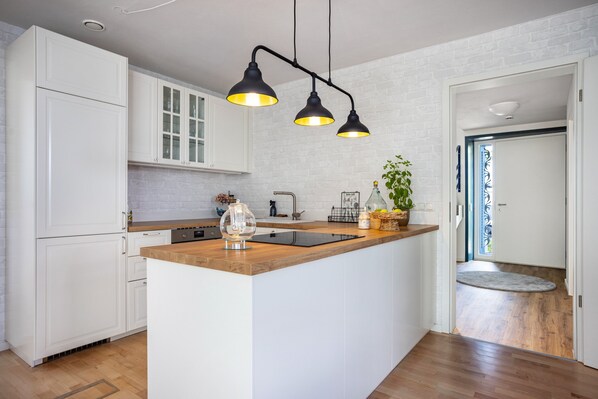 A modern kitchen with white cabinets, a wooden countertop, a built-in island, and black pendant lights.