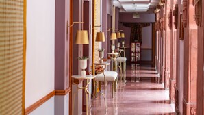 Corredor de hotel com um banco, mesas, cadeiras e um espelho.