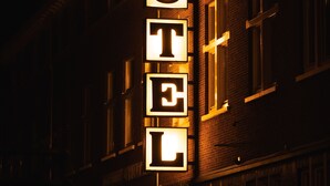 Placa de hotel com letras iluminadas que formam a palavra 'HOTEL' em frente a uma fachada de tijolos à noite.