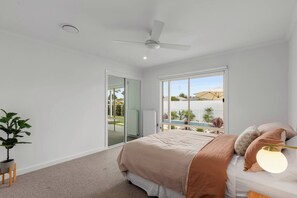 Ein Schlafzimmer mit Bett, Deckenventilator, Topfpflanze und Blick auf einen Swimmingpool.
