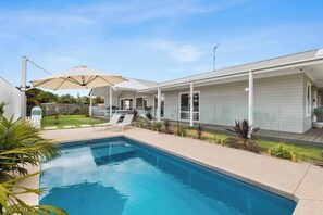 Ein Swimmingpool mit Liegestühlen, eine überdachte Terrasse und ein Haus mit Garage.