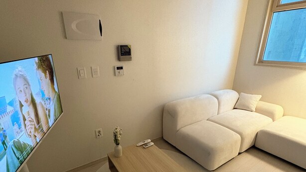 Un salon moderne avec un téléviseur à écran plat, une table basse en bois, un canapé blanc et une petite plante.