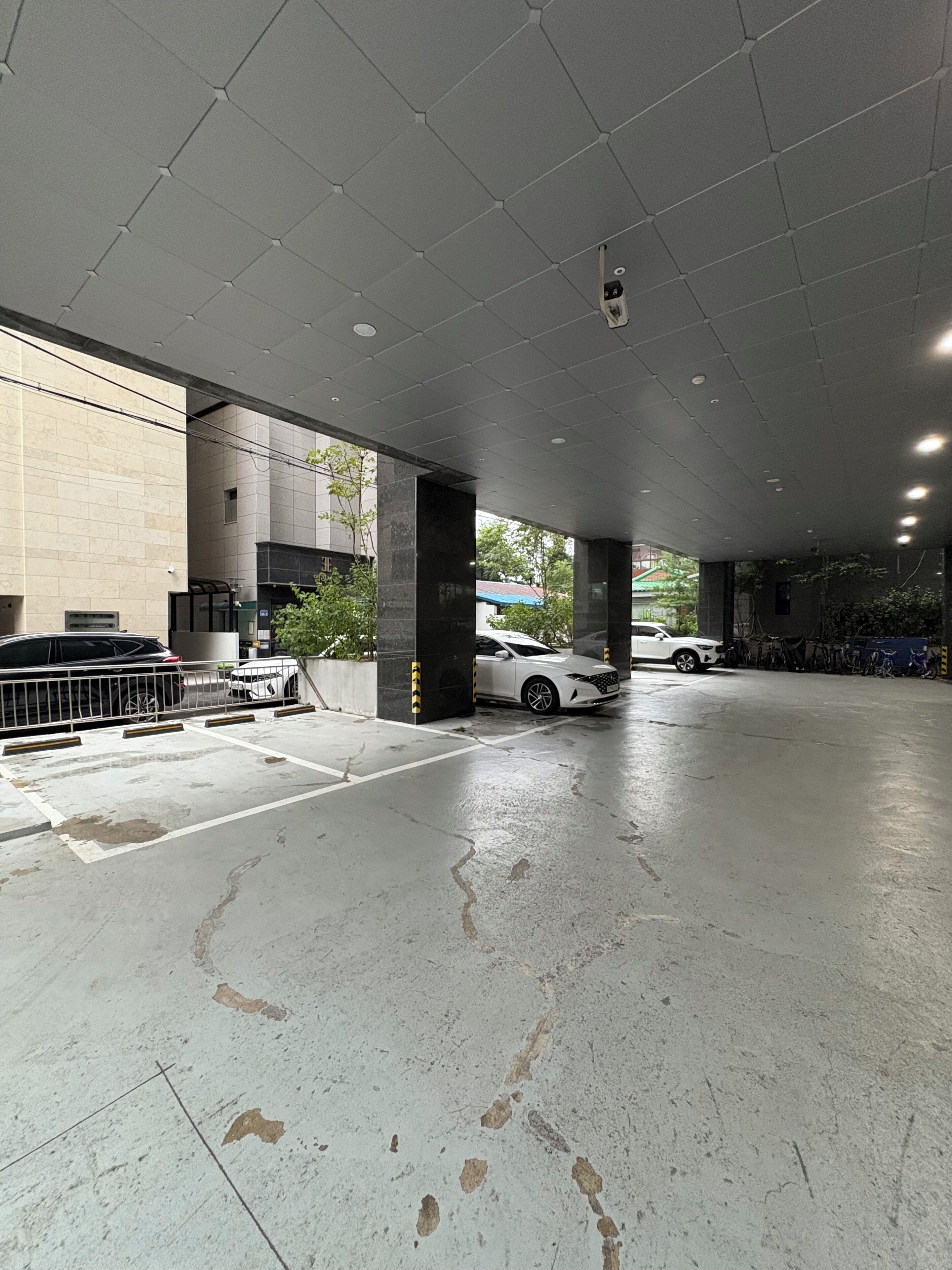 Un parking avec des planchers et des piliers en béton, une voiture blanche garée, et un bâtiment avec un toit végétalisé en arrière-plan.
