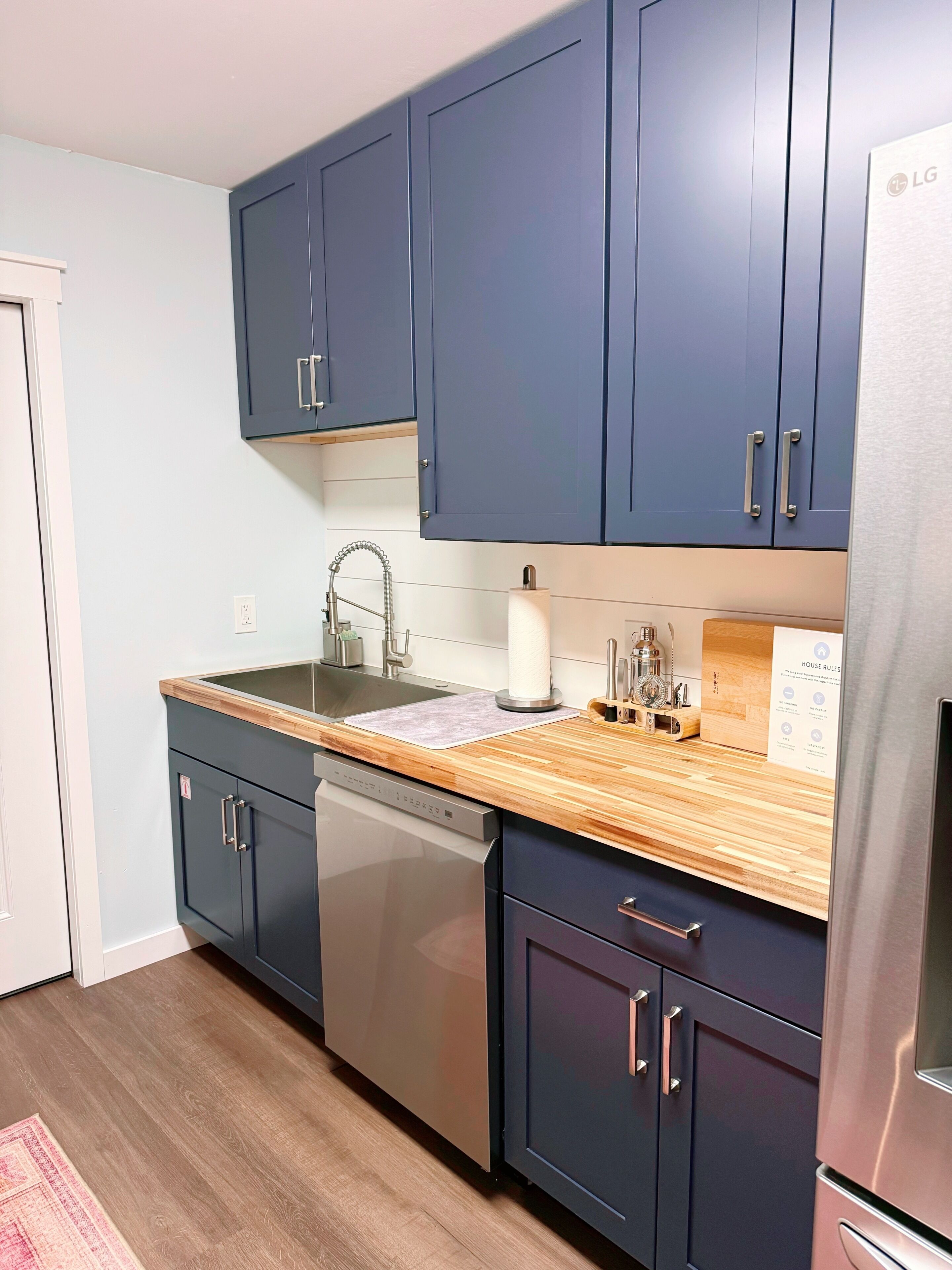 A modern kitchen with dark blue cabinets, stainless steel appliances, and a wooden countertop.