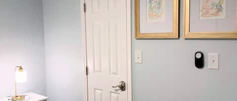 A bedroom with a bed, bedside table, lamp, door, and two framed pictures on the wall.