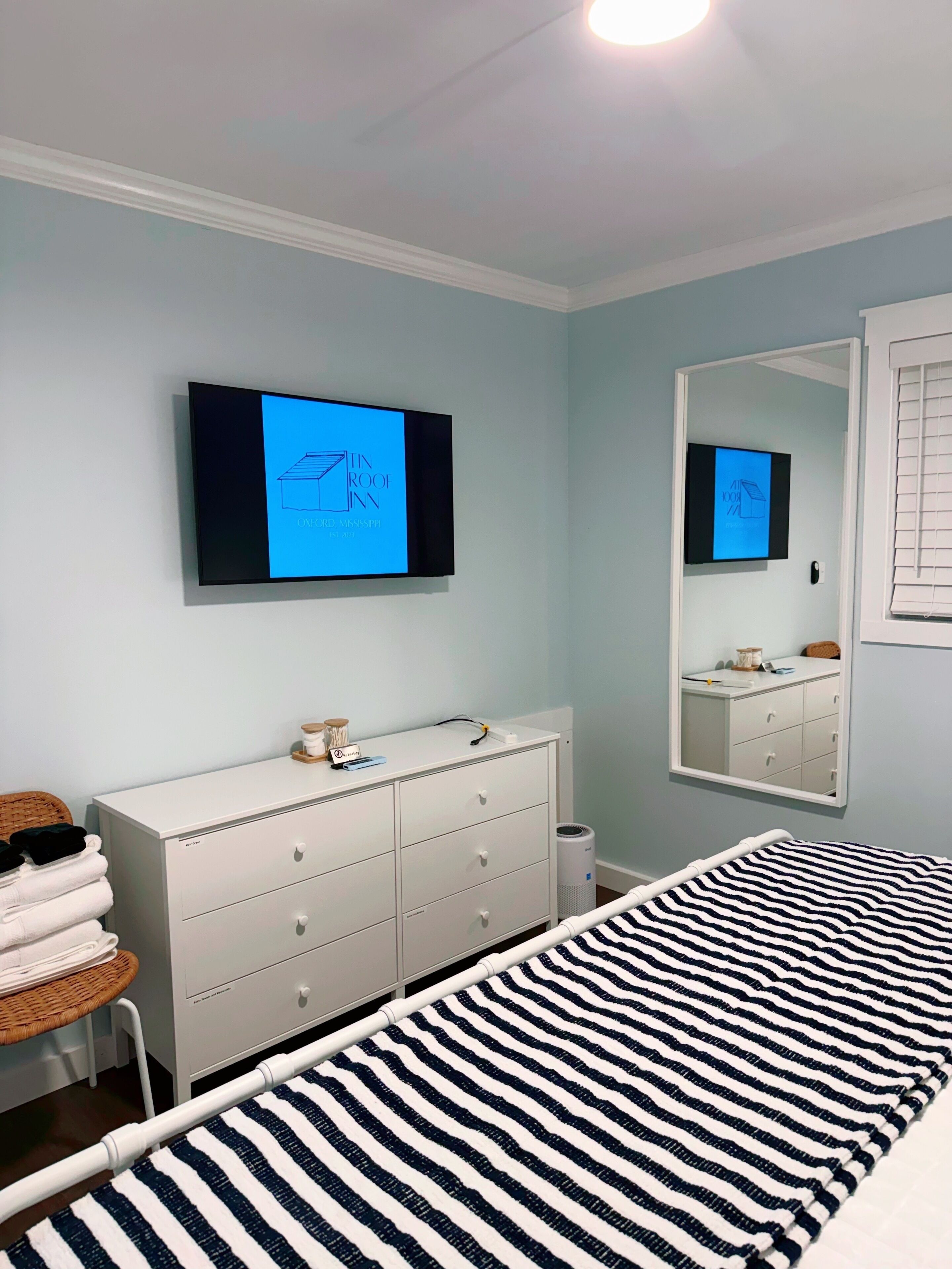 Un dormitorio con cama, cómoda, televisor montado en la pared y espejo.