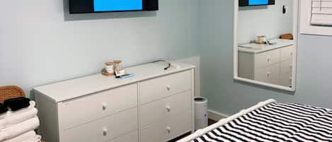 Un dormitorio con cama, cómoda, televisor montado en la pared y espejo.
