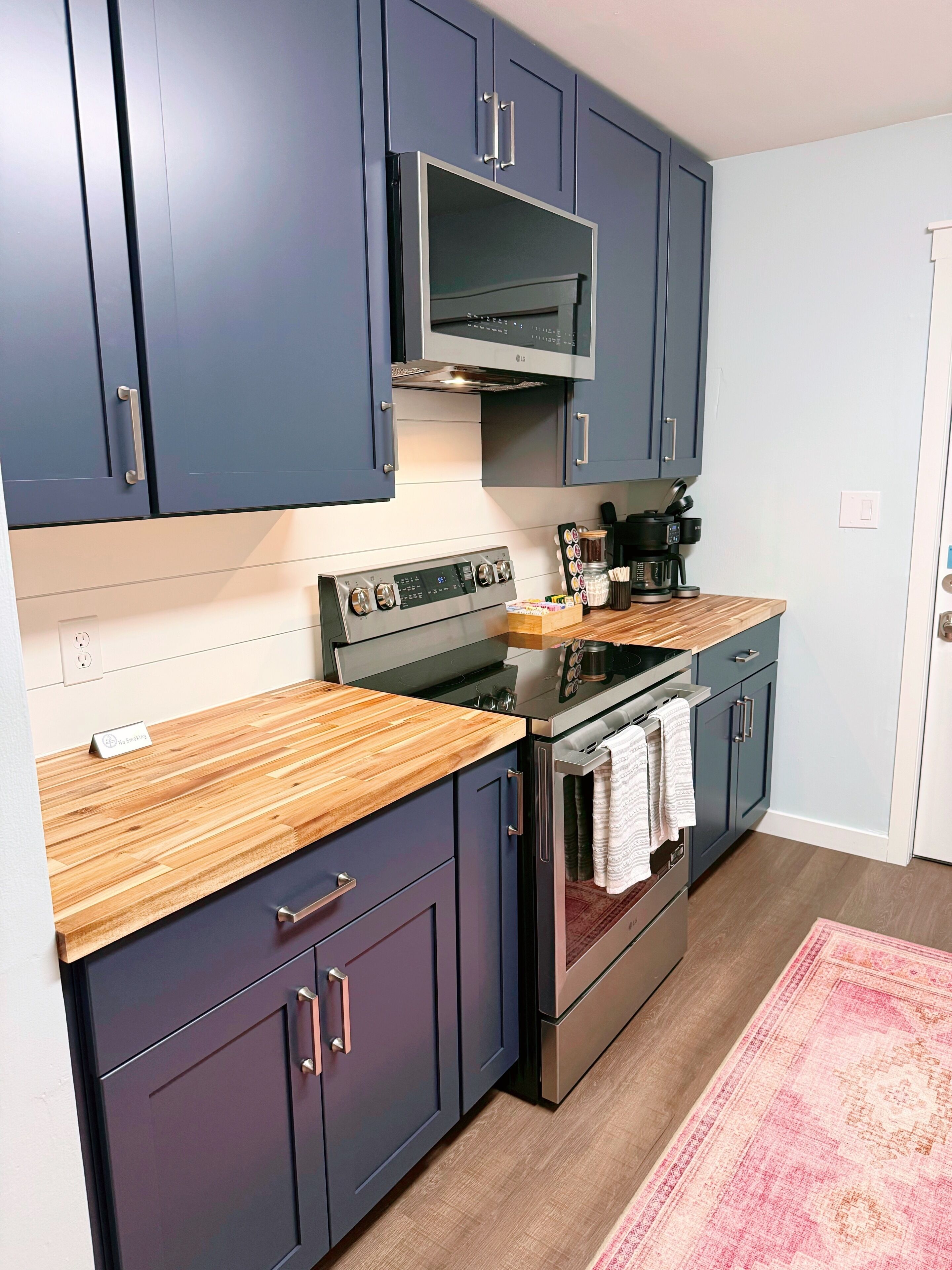 A modern kitchen with dark blue cabinets, a stainless steel stove, and a wooden countertop.