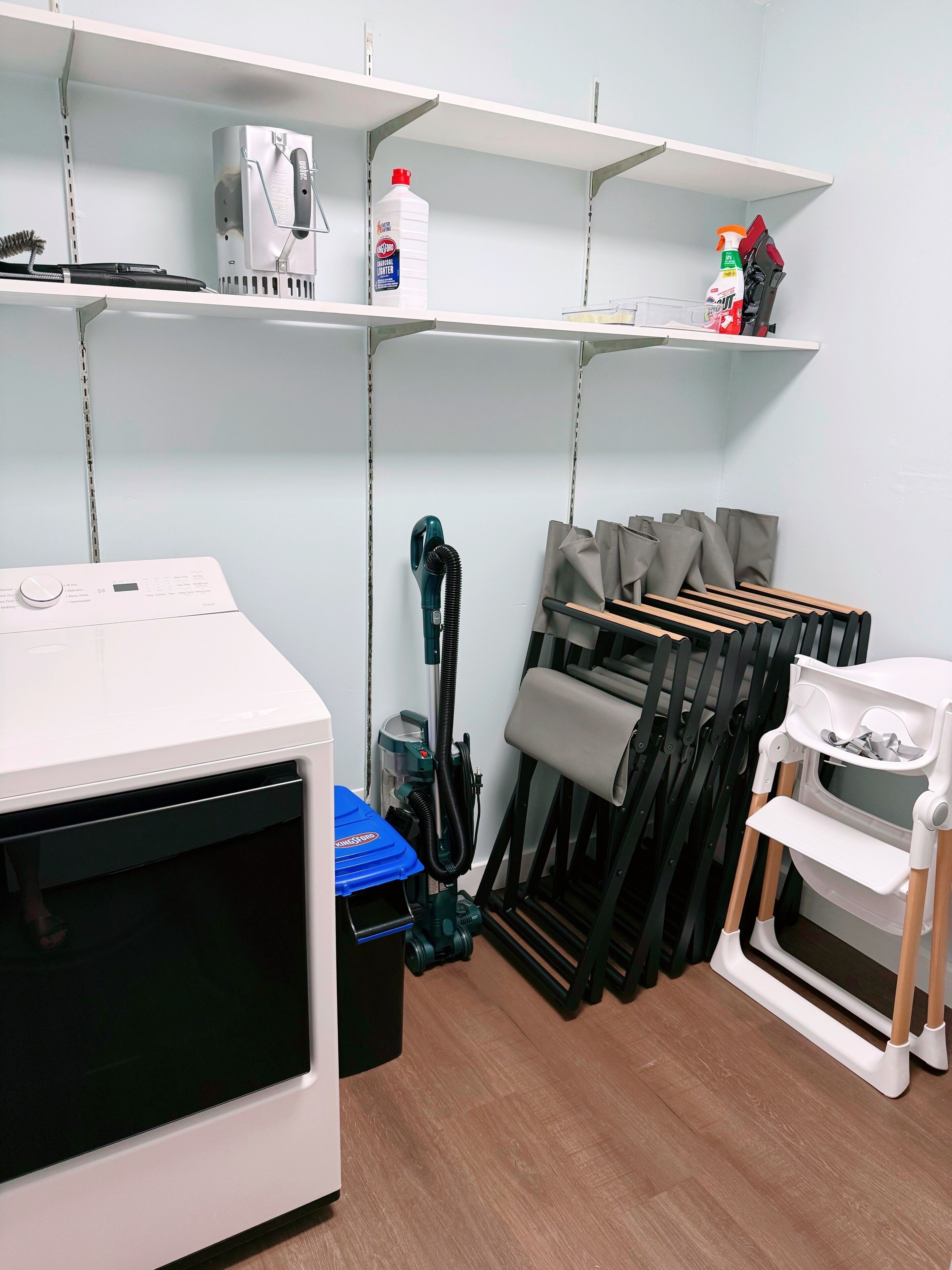 A laundry room with a washing machine, a vacuum cleaner, and a drying rack.