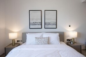 Ein Hotelzimmer mit einem Bett, zwei Nachttischlampen und zwei gerahmten Bildern an der Wand.