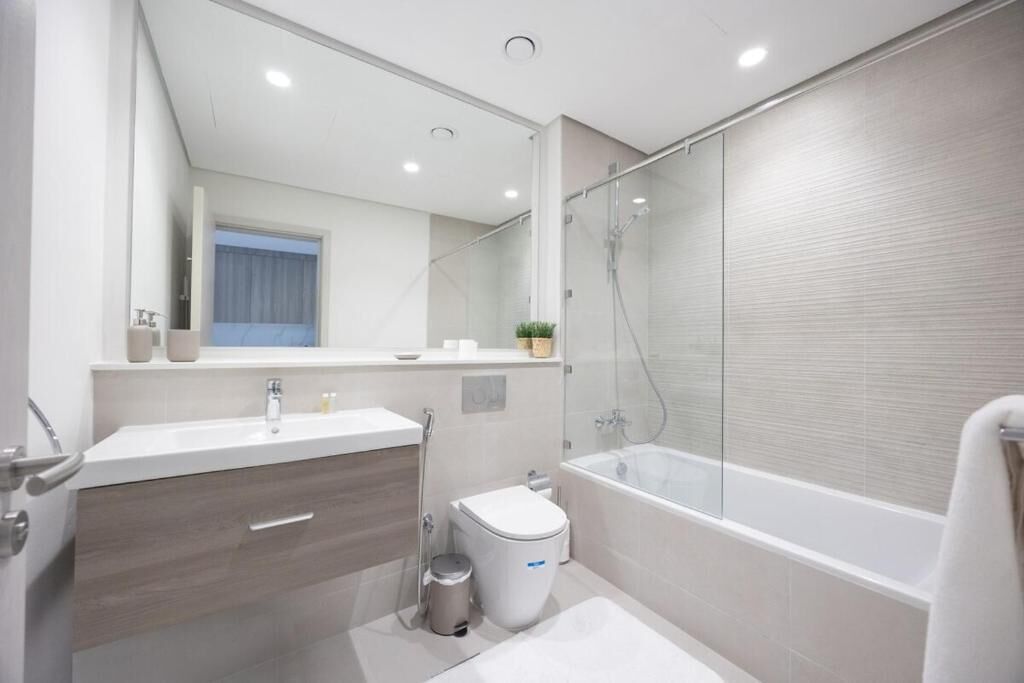 A modern bathroom with a glass-enclosed shower, a white toilet, and a vanity with a mirror.