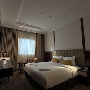 A hotel room with a large bed, a desk, a chair, and a window with curtains. - Park Plaza Hotel (Makkah)