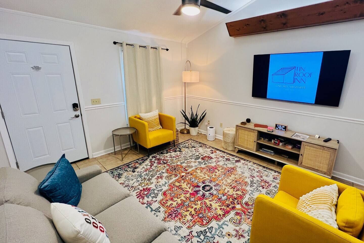 A living room with a sofa, yellow armchairs, a patterned rug, a TV, and a wooden cabinet.