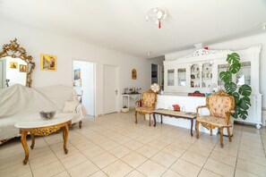 Ein Wohnzimmer mit einem weißen Sofa, zwei verzierten Sesseln, einem kleinen Tisch und einem weißen Schrank mit Glastüren.
