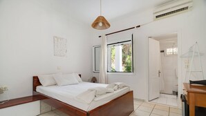 Een slaapkamer met een houten bed, een nachtkastje, een hanglamp, een raam met gordijnen en een deur naar een andere kamer.
