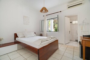 A bedroom with a wooden bed, a bedside table, a hanging light fixture, a window with curtains, and a door leading to another room. - 'Ground Floor' Room, Shared Pool and Wi-Fi (Nikiana)