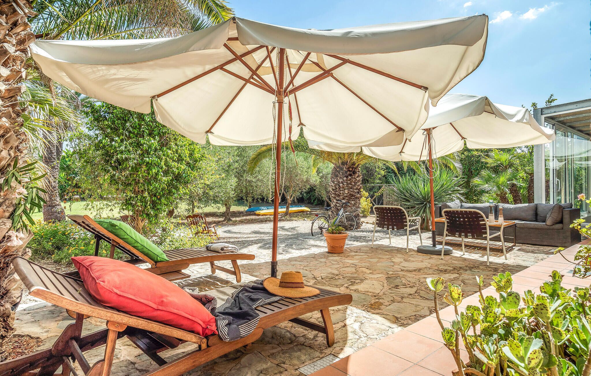 An outdoor seating area with wooden lounge chairs, a sofa, and a large umbrella providing shade.