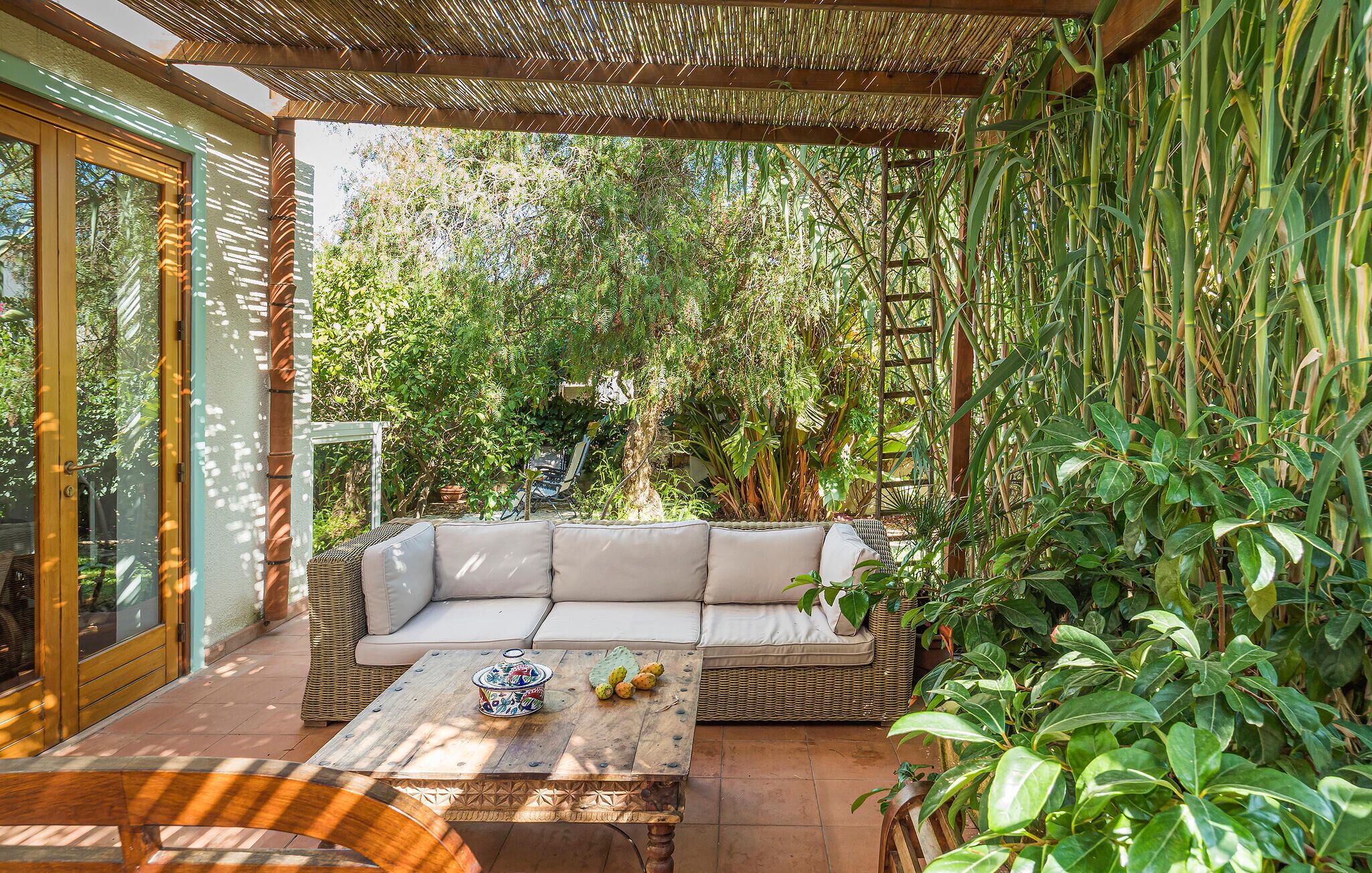 A covered patio with a sofa, a table with fruit, and lush greenery.