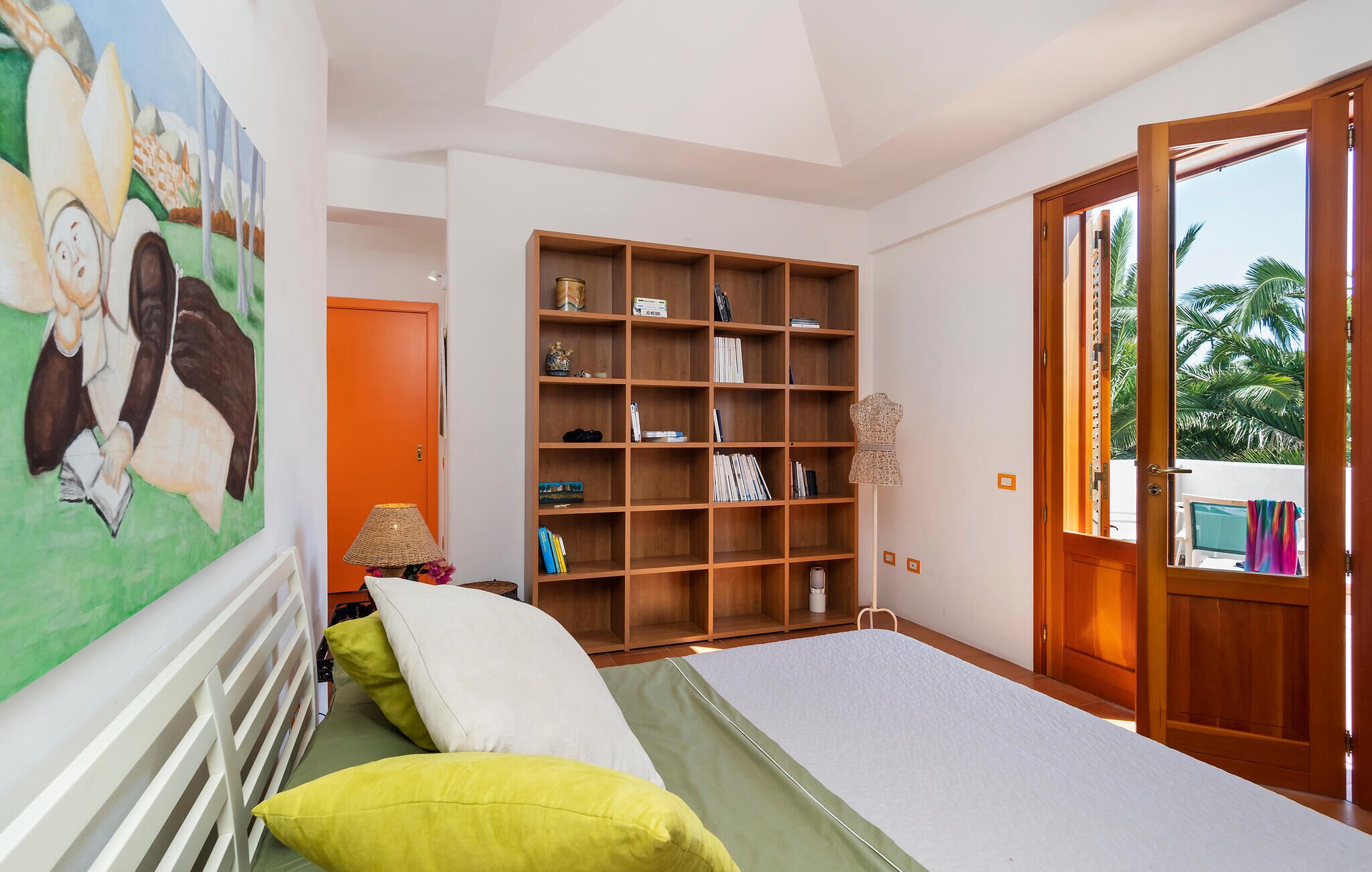 Un dormitorio con una cama, una estantería, un cuadro y una puerta que da a un balcón.