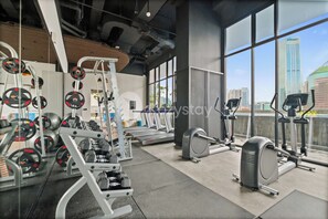 Ein Fitnessstudio mit unterschiedlichen Trainingsgeräten, großen Fenstern und Blick auf die Stadt.