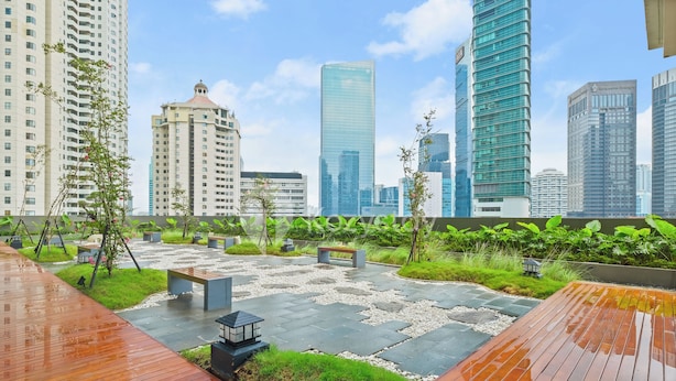 Un jardín en la azotea con terraza de madera, zonas de estar y vistas a edificios altos circundantes.