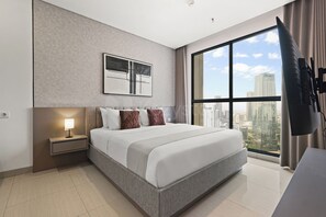 Ein modernes Hotelzimmer mit einem großen Bett, einem Nachttisch mit Lampe, Blick auf die Stadt durch ein großes Fenster und einem an der Wand montierten Fernseher.