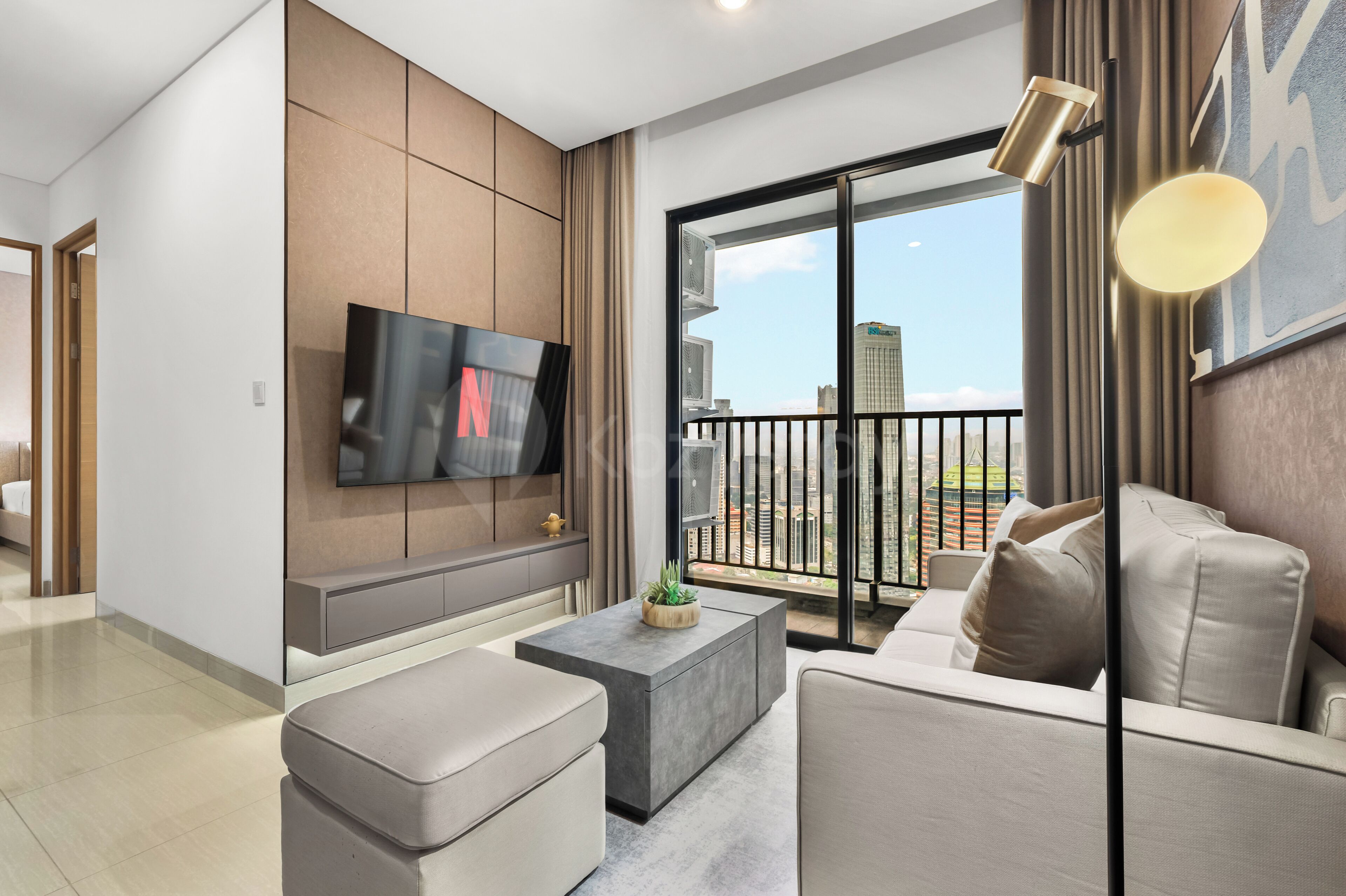 A modern living room with a flat-screen TV, a sofa, a coffee table, and a balcony with a city view.