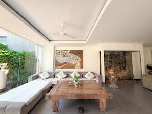 A modern living room with a sofa set, a wooden coffee table, and a ceiling fan. - Villa Alexia in Seminyak - 5 minutes walk to Beach (Seminyak)