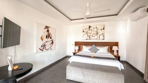 A hotel room with a bed, a ceiling fan, artwork on the walls, a television, and a small table with a vase. - Villa Alexia in Seminyak - 5 minutes walk to Beach (Seminyak)