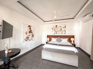 A hotel room with a bed, a ceiling fan, artwork on the walls, a television, and a small table with a vase. - Villa Alexia in Seminyak - 5 minutes walk to Beach (Seminyak)