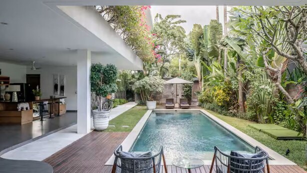 A modern outdoor pool area with a wooden deck, seating, and lush tropical vegetation. - Villa Alexia in Seminyak - 5 minutes walk to Beach (Seminyak)