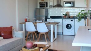 A modern living room with a sofa, dining table, chairs, and a coffee table. The kitchen area includes a microwave, oven, and washing machine. - Corporate Stays First Living - 407 (Asunción)