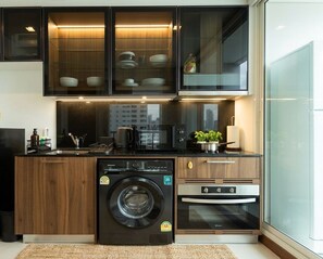 A compact kitchen with a washing machine, oven, and a glass cabinet above the sink. - Best location: less than 5 mins to thonglor bts! gym/swimming pool access. (Krung Thep Maha Nakhon)