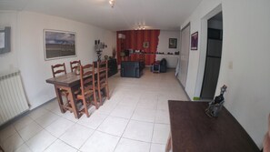 Ein Essbereich mit Tisch und Stühlen, eine Küchenzeile mit Kühlschrank sowie ein Wohnbereich mit einer Couch.