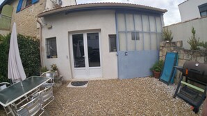 Ein kleines Haus mit Terrasse, einer Schiebetür, einem Grill und einem Tisch mit Stühlen.