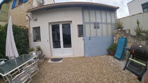 Ein kleines Haus mit Terrasse, einer Schiebetür, einem Grill und einem Tisch mit Stühlen.