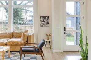 A living room with a beige sofa, a black leather chair, a small table, and a door with a view of the outside. - Sleeps 16 • 2 Nashville Townhomes Near Broadway + Downtown | Lischey & The Stage (Nashville)