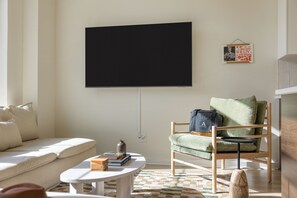 En stue med sofa, grøn lænestol, sofabord og et fladskærms-tv monteret på væggen.