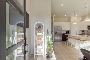Una cocina moderna con gabinetes blancos, una isla central con taburetes altos y una planta en maceta.