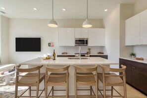 A modern kitchen with a central island, bar stools, white cabinets, a microwave, and pendant lighting. - Sleeps 16 • 2 Nashville Townhomes Near Broadway + Downtown | Lischey & The Stage (Nashville)