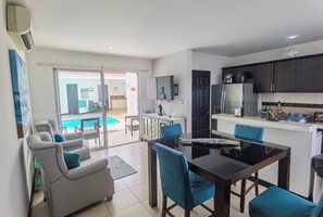 Une cuisine moderne avec des meubles de couleur sombre, une table à manger entourée de chaises bleues, et une piscine visible à travers la porte vitrée.
