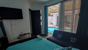 A bedroom with a bed, a TV mounted on the wall, a small table with a bottle, and a sofa with 'hello fall' pillows. - Acogedora casa de playa, Condominio Malaga Bejuco (Bejuco)