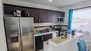 A modern kitchen with stainless steel appliances, dark wooden cabinets, a microwave, and a small island with a sink. - Acogedora casa de playa, Condominio Malaga Bejuco (Bejuco)
