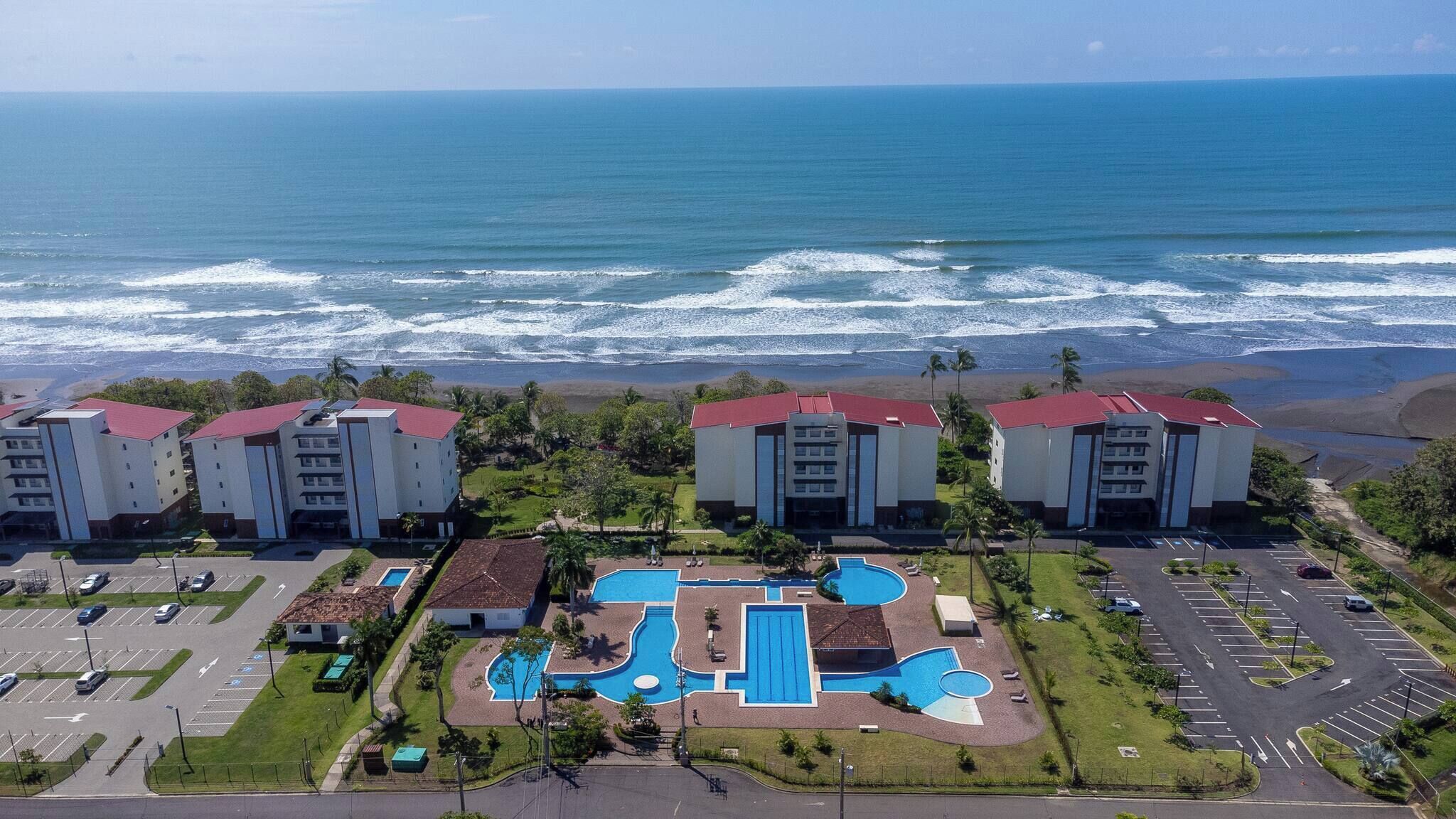 A beachfront hotel with multiple buildings, a swimming pool area, and a parking lot.