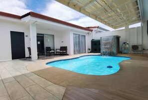 Une piscine à bord incurvé, un patio couvert et une sculpture en pierre.