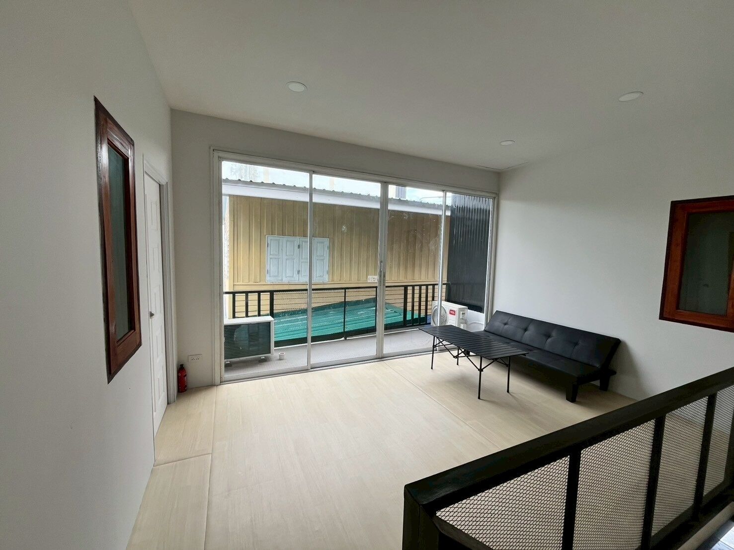 A room with a balcony, a sliding glass door, a black sofa, and a small table.